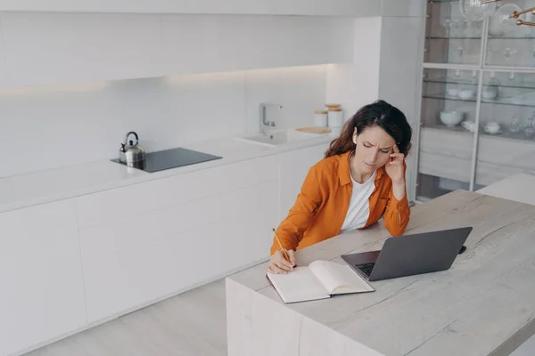 Tired spanish woman is taking notes at online conference. Teacher has stress and fatigue from lesson. Remote student sitting at home and having class via zoom. E-learning on quarantine.