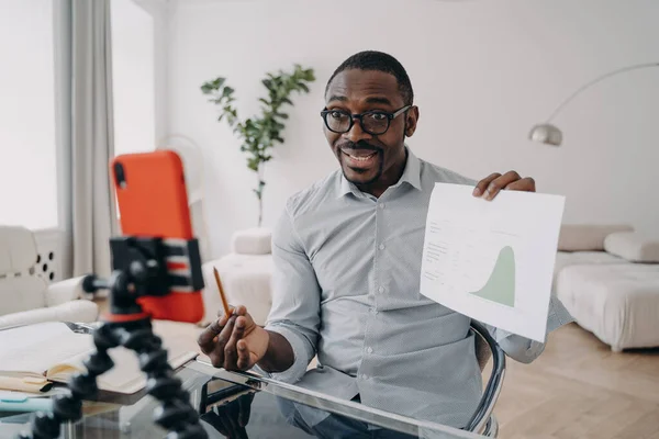 African american man economist showing data graph presenting to business partner via video call on smartphone. Black male businessperson coach discussing work project online with coworkers.