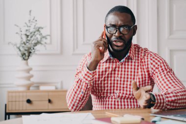 Memnuniyetsiz Afrikalı Amerikalı iş adamı, iş yerinde çalışırken cep telefonuyla konuşurken, telefonda tartışan kızgın girişimci.