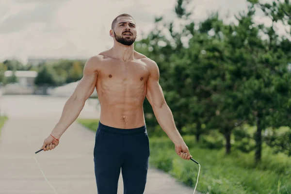 激しいフィットネストレーニングプログラムに集中して裸の胴を持つアスレチックやる気のある男は ロープをスキップする上でジャンプし 公園内のポーズは スポーティボディを持って深く空気を呼吸します 朝のトレーニングコンセプト — ストック写真