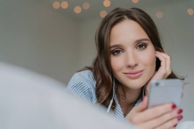 Oldukça koyu saçlı kadın spneds serbest zaman en sevdiği şarkıyla samimi shot modern cep telefonu tutan, doğrudan kameraya benziyor, kapalı teşkil etmektedir, yapmak vardır. Çekici kız yeni melodiler arar