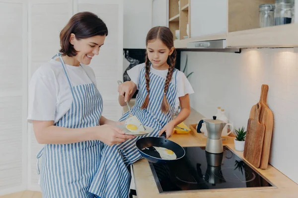 Photo Cheerful Busy Mum Her Daughter Pose Stove Serve Breakfast — Foto Stock