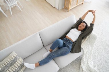 Young woman lying on comfy sofa. Smiling girl stretching body awaking after sleep on cozy couch breath fresh air inside modern living room, enjoying leisure, break, weekend. Recreation, stress relief.