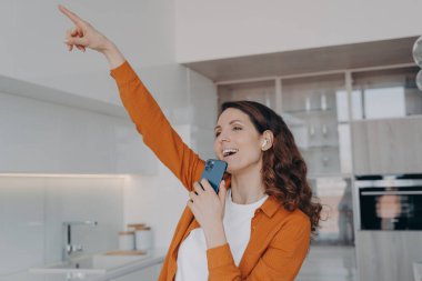 Favourite song karaoke singing at home. Happy caucasian woman in airpods is singing with mobile telephone as with microphone. Girl having fun, relaxing and dancing. Online music listening.