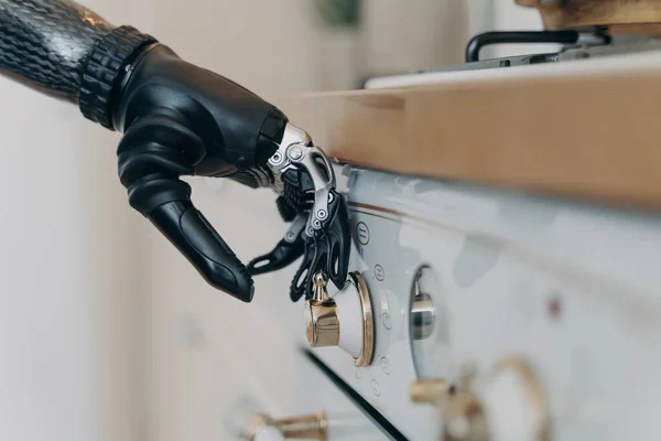 Carbon prosthetic hand of disabled person is switching a stove on at kitchen. Amputee with high technology artificial arm at home. Functions of modern bionic prosthesis. Routine of disabled person.