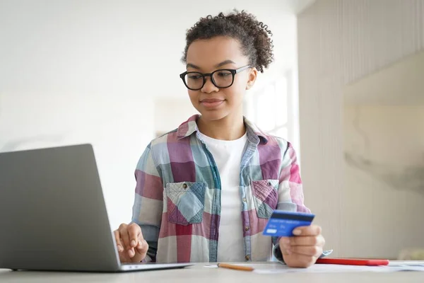 Internet banking application or website. Handsome african american girl is buying online with credit card at home. Happy teenager spends money through internet. Online ordering and shopping.