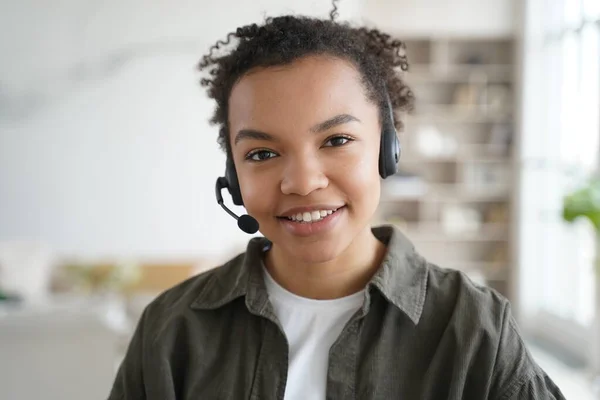 Smiling biracial young female student in headset with microphone learning foreign language online, friendly african american teen girl in headphones looking at camera. Distance education, e-learning.
