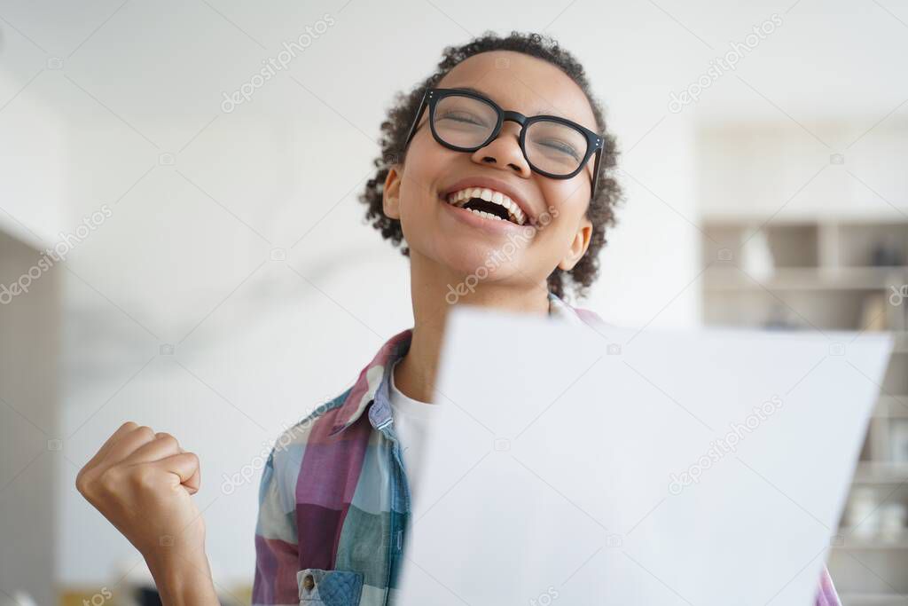 Exam is passed successfully. Overjoyed african american girl holding letter from university. Teenage girl is accepted to college and celebrating her victory. Goal achievement and victory concept.
