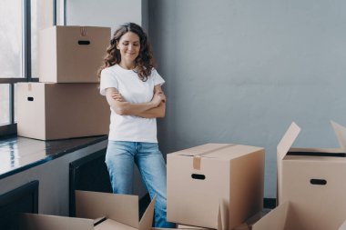 Satisfied woman unpacking boxes. Attractive girl in new apartment. Young woman in jeans and white t-shirt. Relocation, delivery service and new apartment concept.