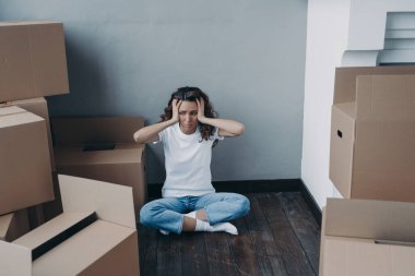 Exhausted young woman amond packed boxes. Anxious girl is holding her head with hands. European woman getting trouble. Stress, headache and depression from moving concept.