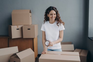 Young woman is packing boxes with duct tape. Lady is wrapping cardboard containers with tape. Moving service worker preparing boxes for shipping. Courier is packing things for and storage.