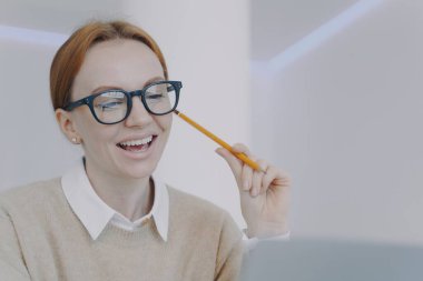 Successful girl is studying online. Happy student holding pencil and taking notes, smiling at camera. Remote study or work concept. Young european businesswoman or employee in office.