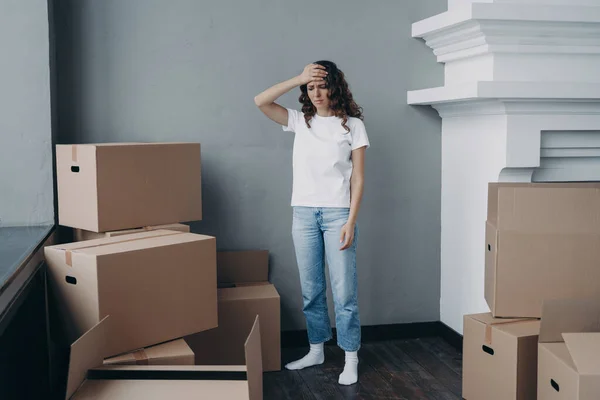 Tired girl is moving. Woman getting headache from boxes packing. Annoyed young lady in jeans and white t-shirt is going to relocate. Homeowner gathering things and getting away from luxurious house.