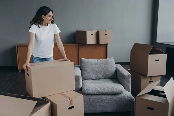 Happy european woman relocates alone. Proud single lady in casual outfit moves. Cardboard boxes on floor. Real estate purchase and mortgage. Delivery service ordering for the boxes unloading.