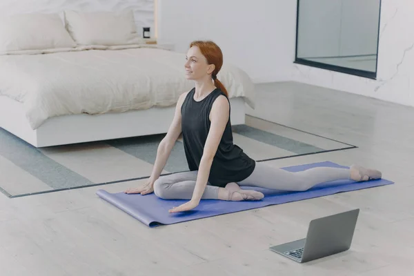 Morning exercises. Young caucasian woman is stretching on mat. Concept of internet learning and home classes. Personal training and gymnastics on quarantine. Home isolation.