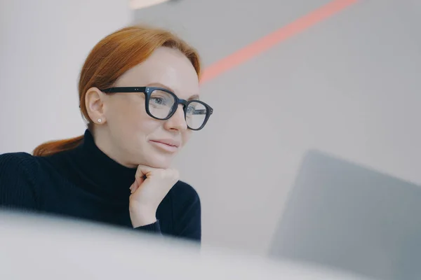 Lady is reading on PC screen. Happy face of confident young woman at workplace in modern office. Positive attractive girl is manager. Businesswoman looking at the display of computer and working.