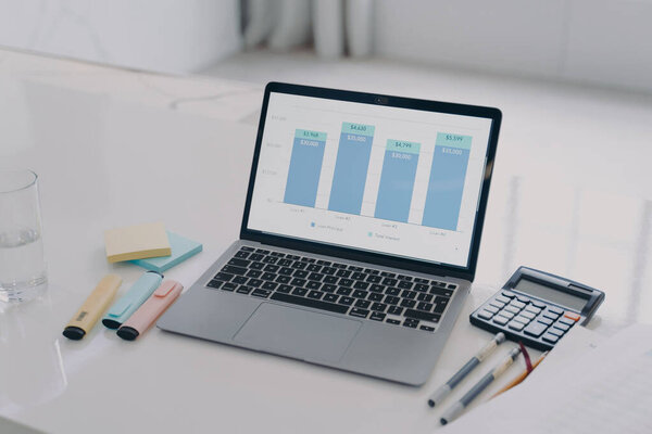 Laptop screen with program opened. PC on desk in office. Bars of graphs on display. Pens on the table. Business presentation and company growth. Data analysis concept.