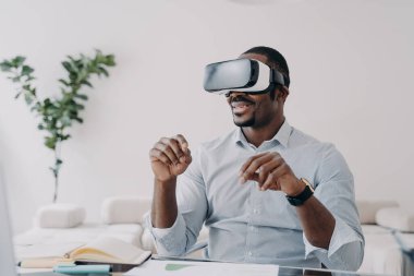 Happy afro guy in vr headset at home. Businessman has virtual meeting. Freelancer is working on startup design project. Modern interactive gadget for distant work and entertainment.