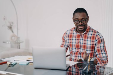 Puzzled african american man reading email working at laptop. Perplexed black male manager looking at computer screen. Broken or discharged device, poor internet connection. Problem at remote work.