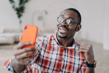 Positive afro man has video call on smartphone. Guy stays home on quarantine and has conversation with friends online. Business talk or corporate discussion through internet. Distance briefing.