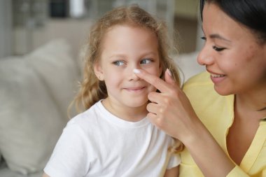 Loving mother touching face nose of small foster daughter. Smiling female feels love to little girl child, enjoy tender moment together at home. Happy motherhood, childcare, adoption of children.