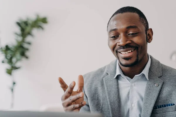 Smiling african american businessman holding a video call with customers on laptop. Optimistic black male businessperson or coach gives online consultation, advises clients.