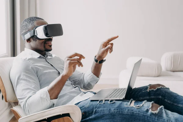 Relaxed businessman clicks virtual buttons. Gestures of african american man in vr glasses. Guy is working at home. Distant work and futuristic gaming. Modern digital technology for business.