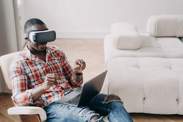 Afro man in vr headset. Workplace at home office. Businessman has virtual meeting. Relaxed freelancer is sitting in chair and working on project. High tech digital technology and vr gaming.