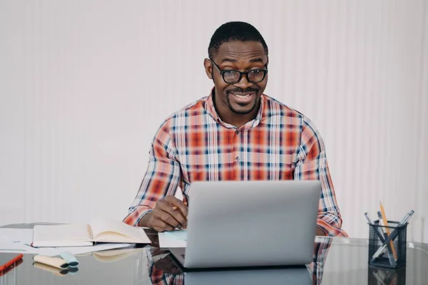 Positive afro man in glasses has online conference on laptop. Businessman gives consultation to client. Teacher has remote lesson with student. Online courses, internet meeting.