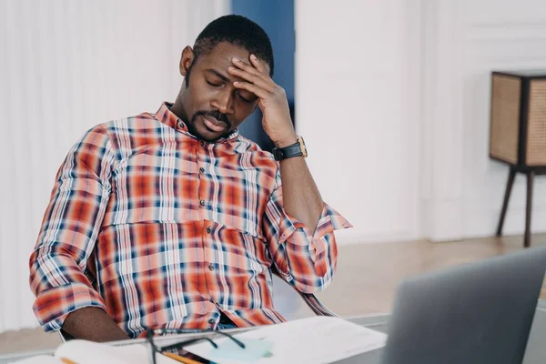 Tired african american businessman suffer from headache at workplace at laptop. Frustrated overworked black male guy touching head thinking about business problem, closed eyes. Stress at work concept