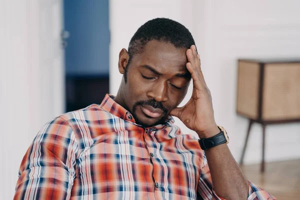 Exhausted african american man touches head suffer from headache or migraine, tired upset black guy with closed eyes feel fatigue due to lack of sleep, problems at work, life crisis.