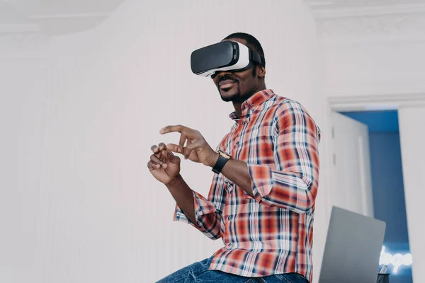 Modern african american man in VR glasses enjoy virtual tour in augmented cyberspace, touch 3d objects, interacting with digital interface. Black guy uses virtual reality goggles for online shopping.