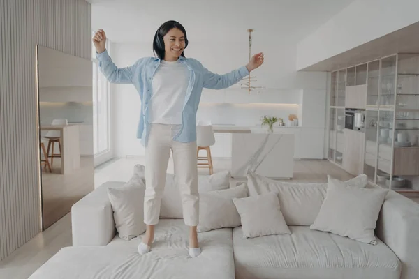 Excited Young Woman Wearing Wireless Headphones Jumping Sofa Alone Home — Foto de Stock