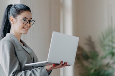 Çalışan şirket çalışanlarının kapalı çekimleri, modern dizüstü bilgisayarı tutuyor, tarihi iletiyor, kablosuz internete bağlanıyor, görsel düzeltme için gözlük takıyor, geri bildirim gönderiyor.
