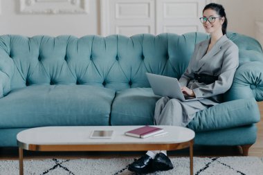 Medya pazarlama şirketinin resmi sitesindeki başarılı genç kadın yönetici sörfleri modern dizüstü bilgisayar kullanıyor, kablosuz internet kullanıyor, rahat kabinede çalışıyor masaüstü bilgisayarlı rahat koltukta oturuyor