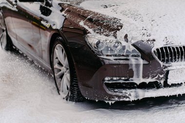 Lavaboda servis edilen siyah arabanın fotoğrafı. Araba yıkamada sabunla kaplı kirli bir otomobil. Profesyonel araba yıkama. Araç temizleme