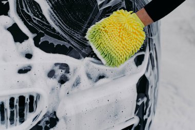 Tanınmayan adam araba istasyonunda sabunlu siyah arabayı bezle yıkıyor. Erkek işçi otomobil temizler. Araç ve servis kavramı