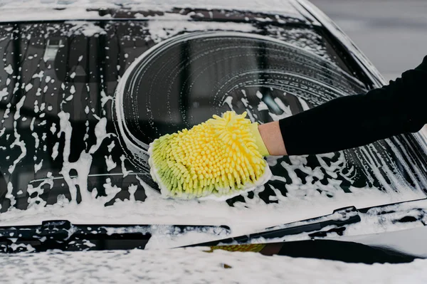 Black dirty car in white soap foam at car wash service station