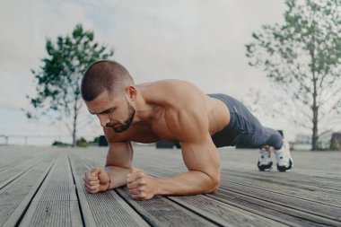 Güçlü sporcuların açık havada çekimleri tahta pozisyonda durur, tüm çabalarını formda ve sağlıklı tutmak için harcar. Konsantre ifade ile sporcu, açık havada egzersiz yapar. Vücut geliştirici basın egzersizi yapıyor