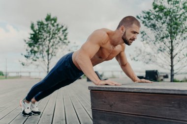 Sporda kendine güvenen kaslı sporcu açık havada şınav çekiyor, pazılar ve trenler üzerinde çalışıyor. Güçlü üstsüz atletik adam açık havada egzersiz yapıyor. İnsanlar, motivasyon, eğitim kavramı