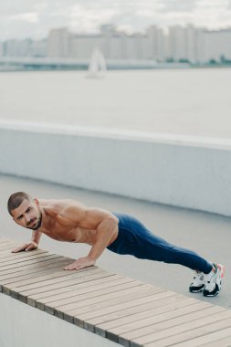 Esnek formda bir adam gezinti güvertesinde kalas egzersizi yapıyor çıplak gövdesi var spor kıyafetleri giymiş yoga antrenmanlarına hazırlanıyor sabahları açık hava trenleri var. Sportif yaşam tarzı