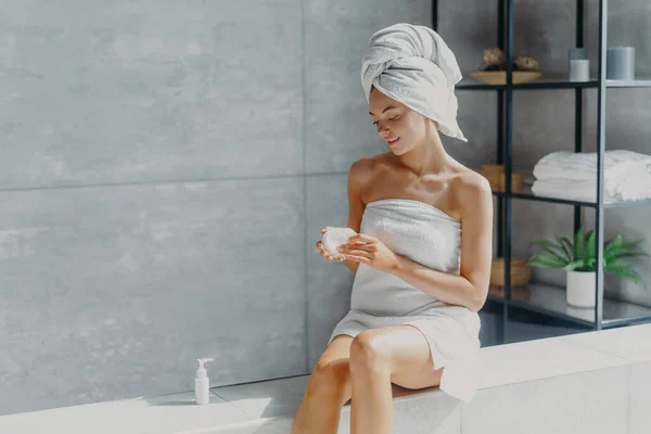 Pleased Healthy Woman Wrapped Bath Towel Applies Body Cream Showering — Foto de Stock