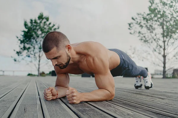 Güçlü sporcuların açık havada çekimleri tahta pozisyonda durur, tüm çabalarını formda ve sağlıklı tutmak için harcar. Konsantre ifade ile sporcu, açık havada egzersiz yapar. Vücut geliştirici basın egzersizi yapıyor
