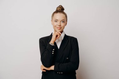 Koyu renk takım elbiseli çekici iş kadını kameraya özgüvenli bir şekilde bakıyor, dinliyor ve fırsatları düşünüyor gri arka planda duruyor.