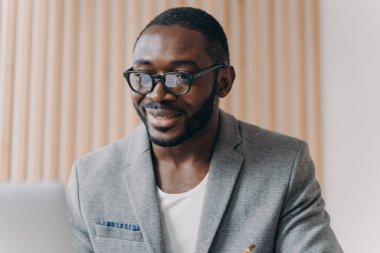 Resmi olarak kendine güvenen genç Afrikalı iş adamının portresi ofiste dizüstü bilgisayarın önünde oturmuş bilgisayar ekranına bakıyor, internette sörf yapıyor. Çeşitli iş insanları kavramı