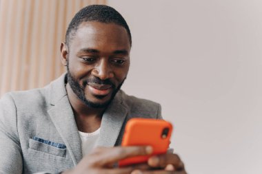 Çekici gülümseyen, resmi takım elbiseli, iş arkadaşlarıyla akıllı telefondan sohbet eden, şirket ofisine e-posta gönderen, iş görüşmesinden önce tatmin olmuş genç Afrikalı serbest çalışan.