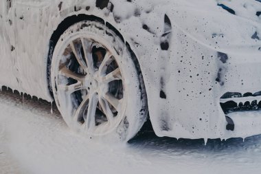 Dış araba temizliği. Araba yıkama istasyonunda beyaz sabun köpüğüyle araba tekerleğini kapat. Deterjanla profesyonel araç temizliği.