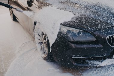 Verimli araç temizliği, araba yıkama merkezindeki yüksek basınçlı çamaşır makinesiyle araçlara deterjan sıkmak. Açık hava araba temizleme konsepti. Manuel dış araba yıkama sırasında köpüklü siyah yüzey