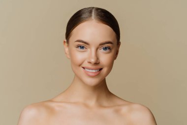 Çekici Avrupalı bir kadının güzel portresi, güzel yüzlü, sağlıklı tenli, bakımlı, gülümseyen, çıplak omuzlarıyla bej arka planda duran, temiz, taze bir cilde sahip.