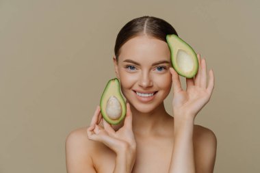 Doğal vitaminlerle yüz bakımı. Memnun esmer kadın hafifçe gülümsüyor. Avokado parçalarını nazikçe tutuyor. Doğrudan kameraya bakıyor..